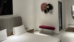 Moderni makuuhuone, jossa on suuri sänky, harmaa pääty, punainen penkki ja ainutlaatuinen seinätaideteos.