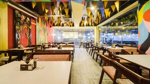 Interior de un restaurante con varias mesas y sillas, un diseño de techo colorido y vistas a través de un separador de vidrio.