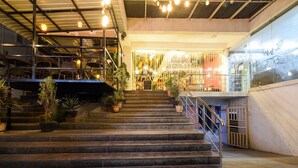Una escalera conduce a un restaurante con mesas al aire libre, plantas en macetas y barandilla de metal.