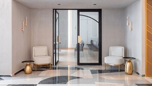 A modern lobby with two seating areas, a glass door leading to a conference room, and a marble floor. - 1910 Legacy Hotel (Volos)