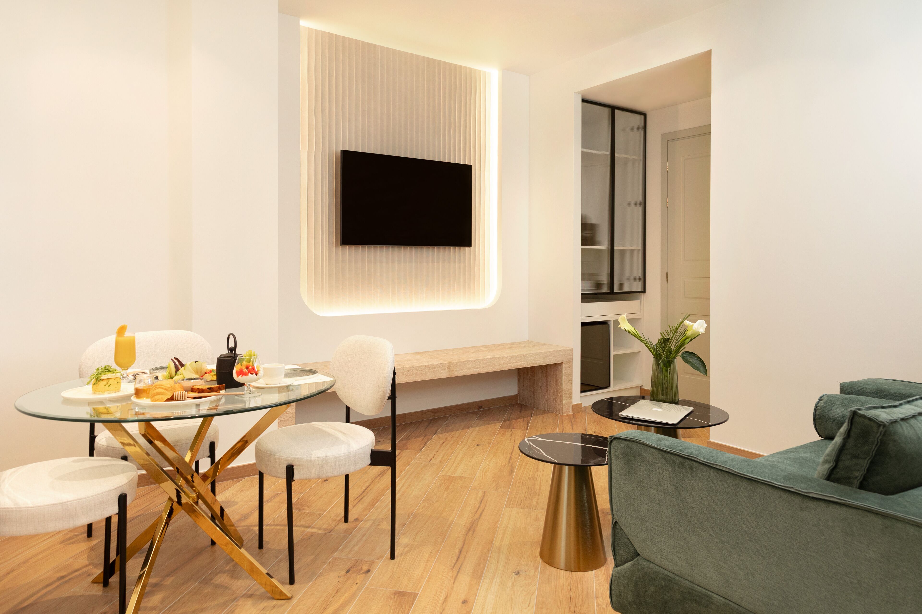 Een moderne woonkamer met een glazen eettafel, een bank en een aan de muur bevestigde televisie.