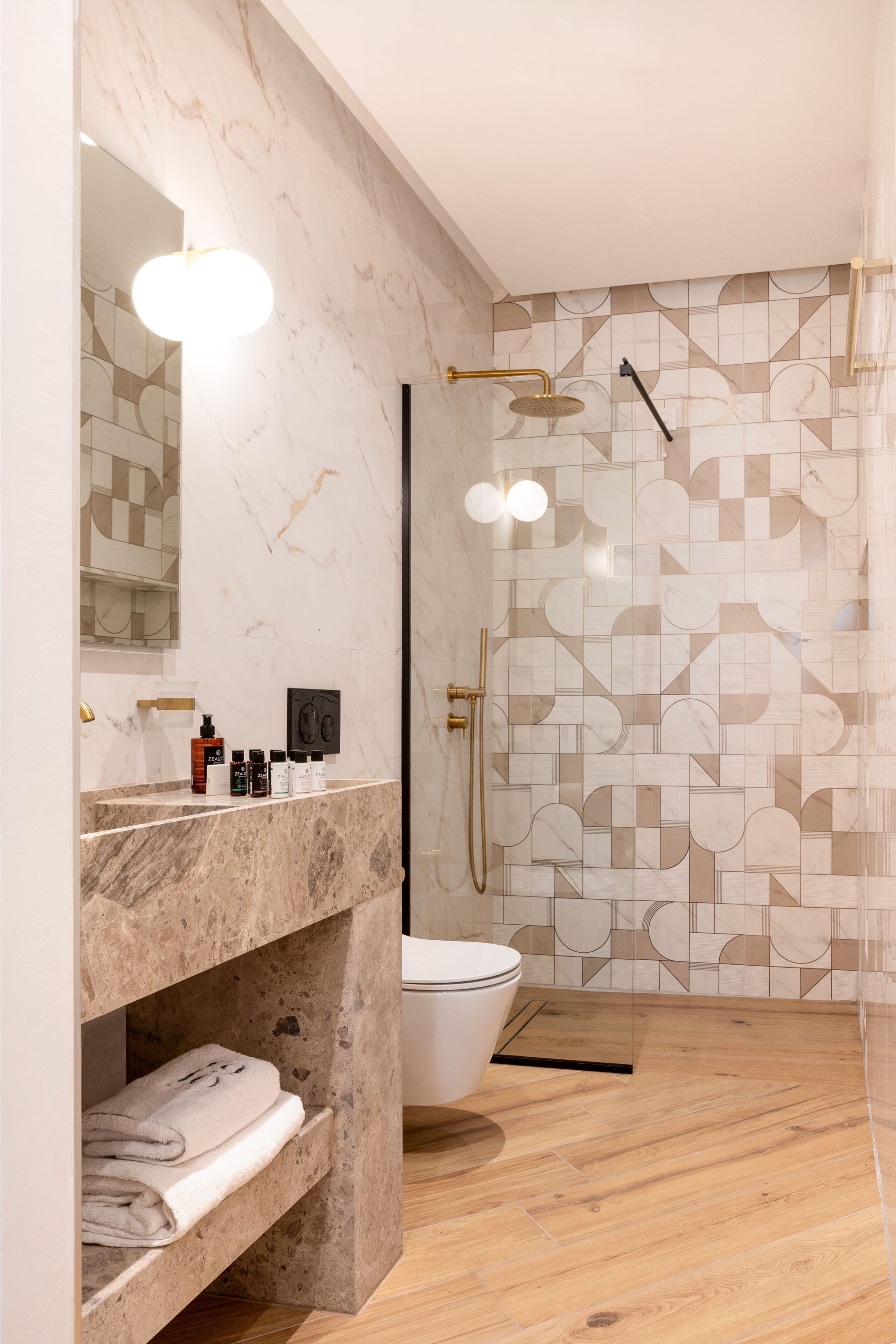A modern bathroom with a marble vanity, a toilet, and a shower with geometric tile patterns.