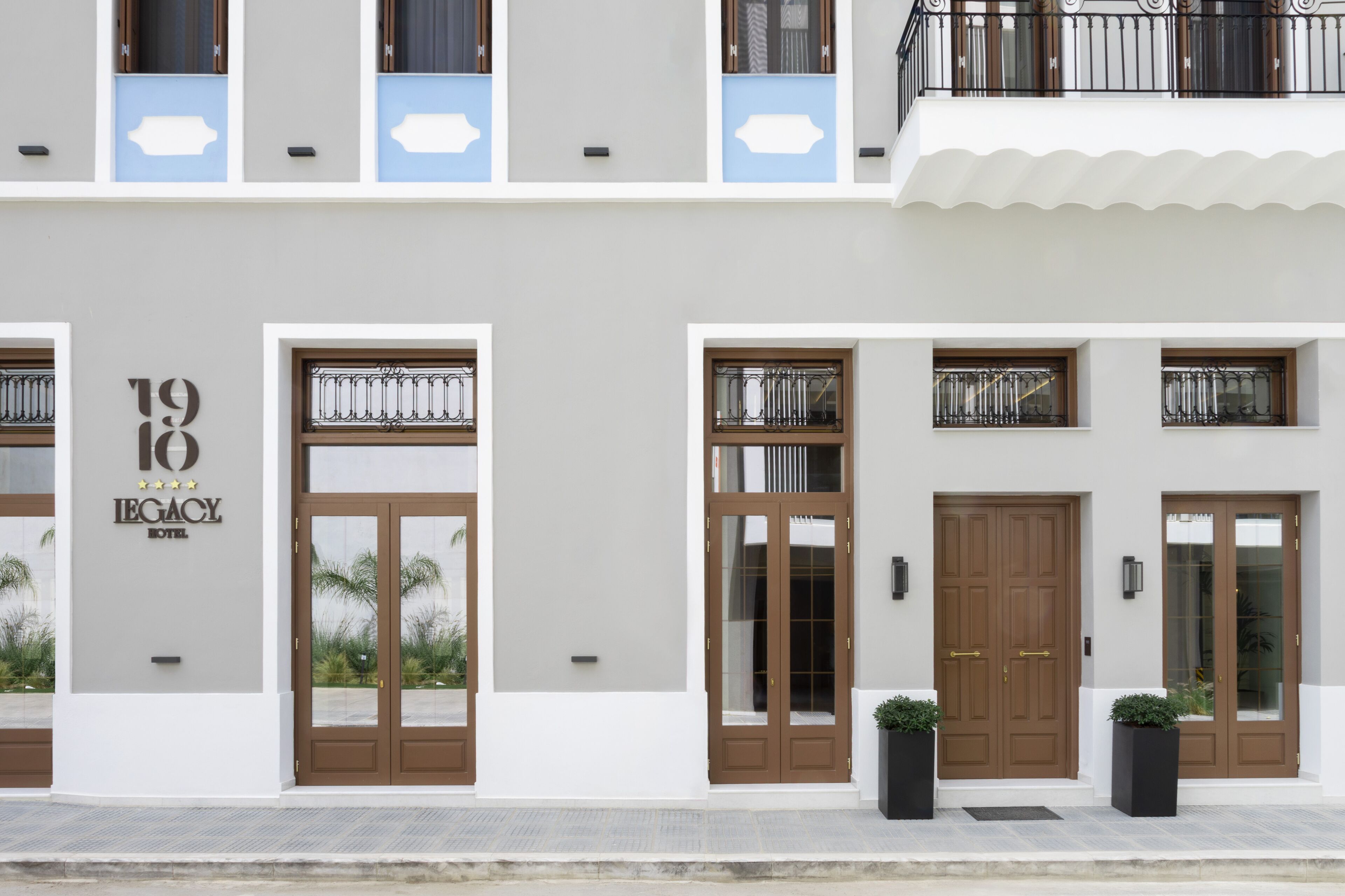 Fachada de hotel com design moderno, exibindo uma grande placa com o número 19, diversas entradas e uma varanda com guarda-corpo.