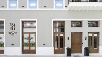 Fachada de hotel com design moderno, exibindo uma grande placa com o número 19, diversas entradas e uma varanda com guarda-corpo.