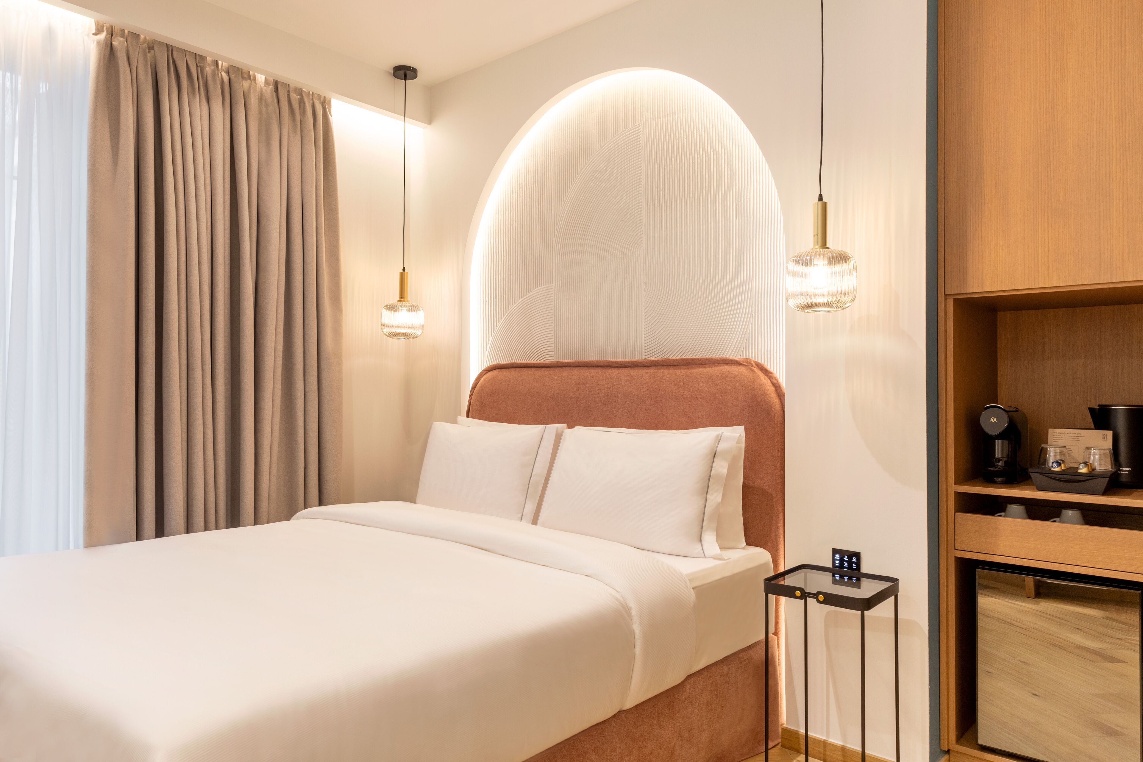 Quarto de hotel com cama, máquina de café e pequena mesa com painel de controle.