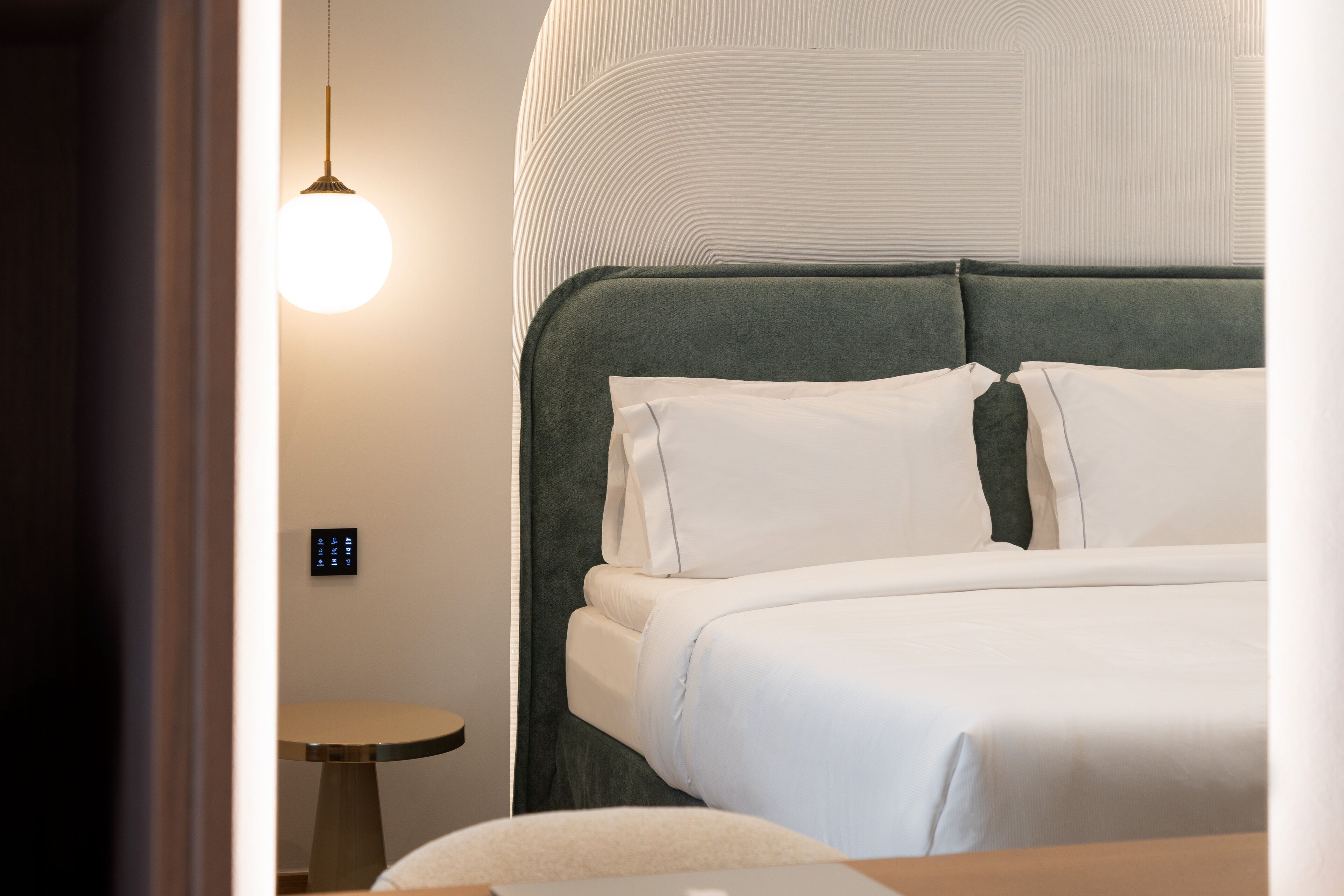 A neatly made bed with white linens and a green upholstered headboard.
