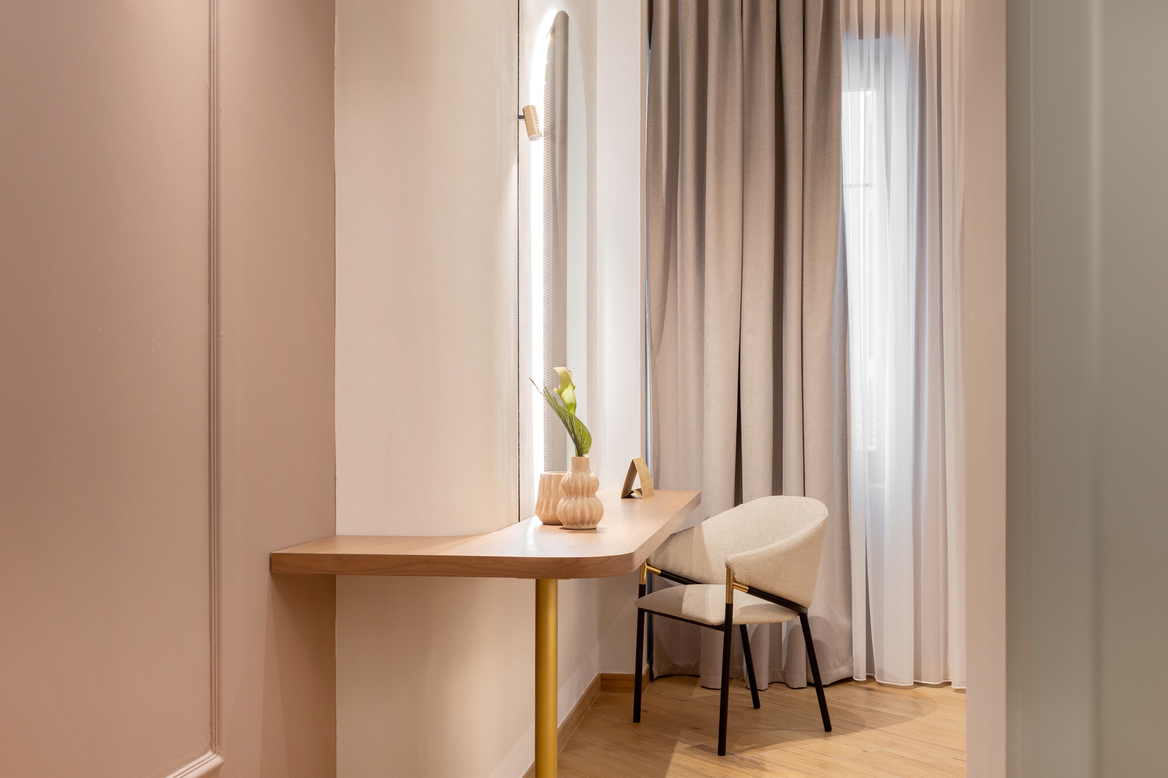 A modern room with a wooden desk, a chair, a vase with a plant, and a window with curtains.