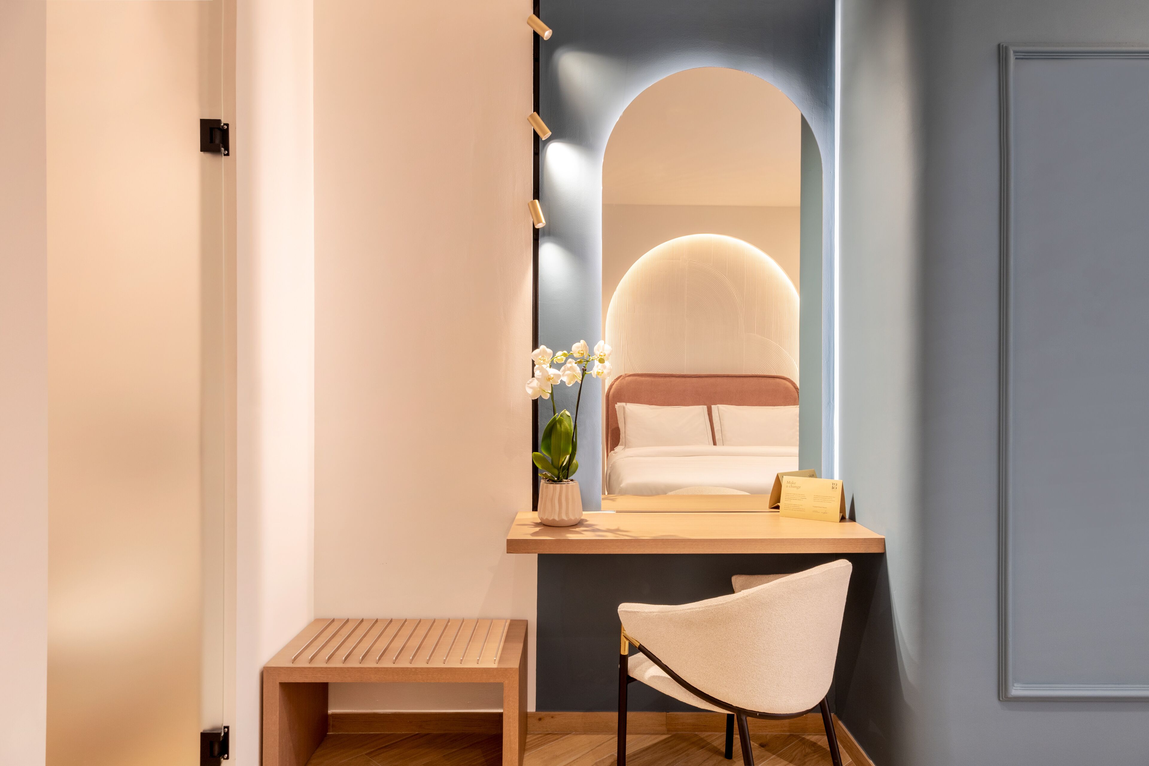 Un baño moderno con tocador de madera, un banco, un espejo y una orquídea en maceta.