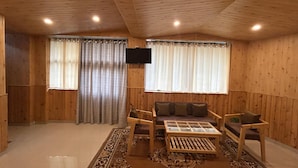 A wooden-paneled room with a sofa, armchairs, a coffee table, and a television mounted on the wall. - Hotel Ganpati (Lohaghat)