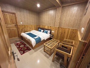 A wooden-paneled room with a bed, a small table, and a chair. - Hotel Ganpati (Lohaghat)