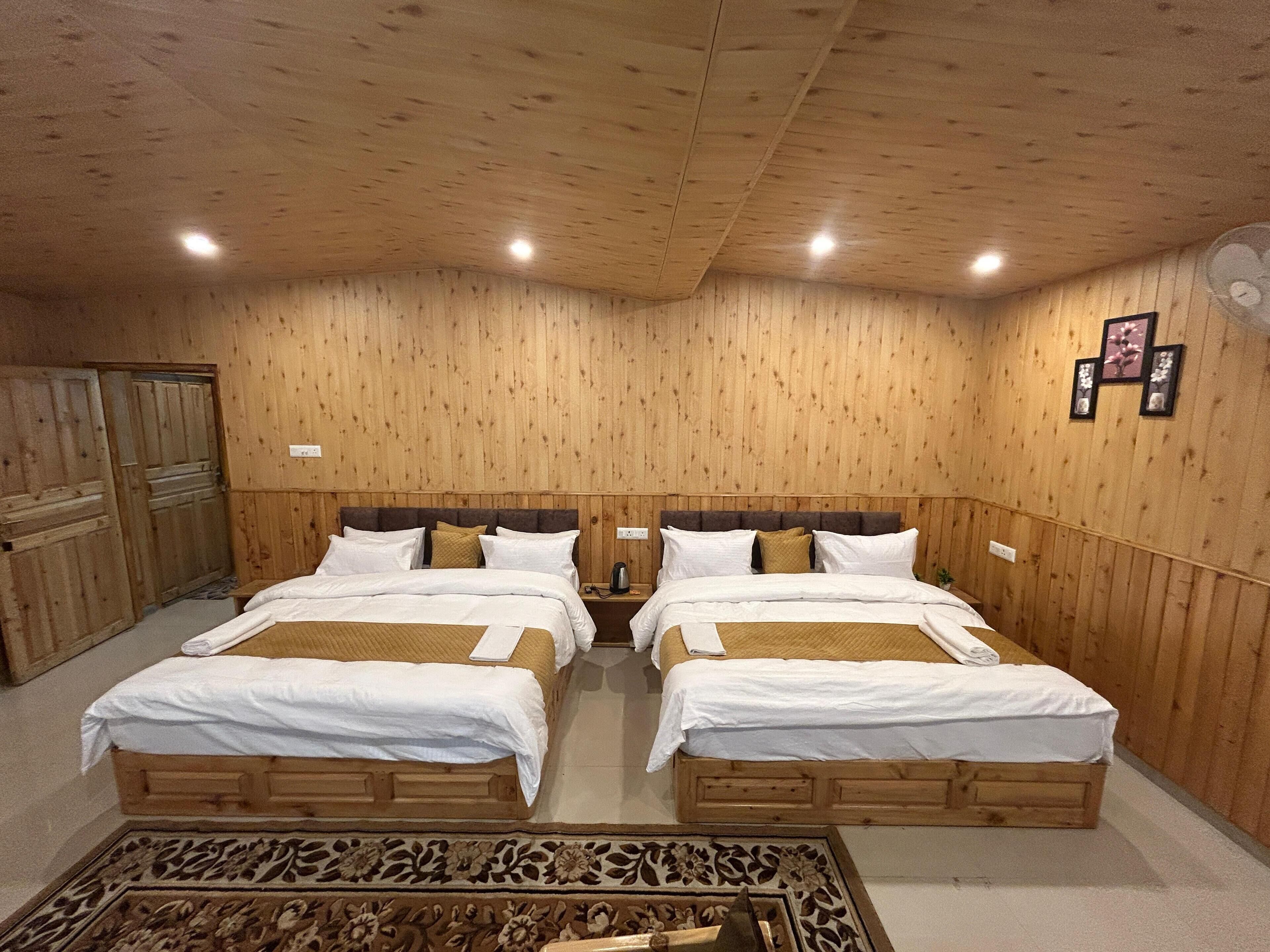 A room with two wooden beds, a patterned rug, and wooden paneling on the walls.