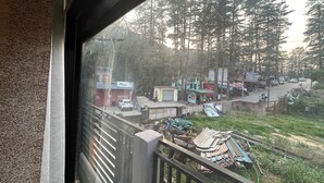 A view from a window overlooking a street with buildings, trees, and parked vehicles. - Hotel Ganpati (Lohaghat)