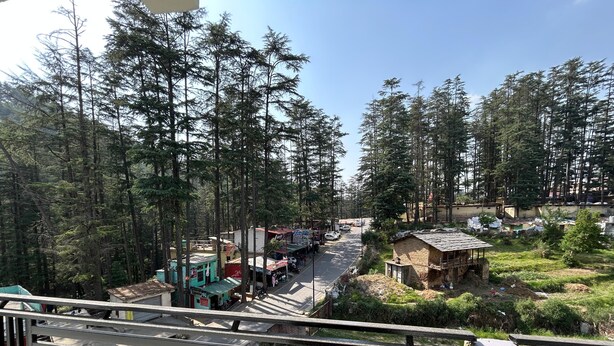 A street scene with buildings, vehicles, and a dense forest in the background. - Hotel Ganpati (Lohaghat)