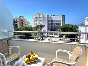 A balcony with white chairs and a table, a wicker basket with fruits, and a view of buildings and trees. - Holiday Apartment in Golem 070 (Durres)