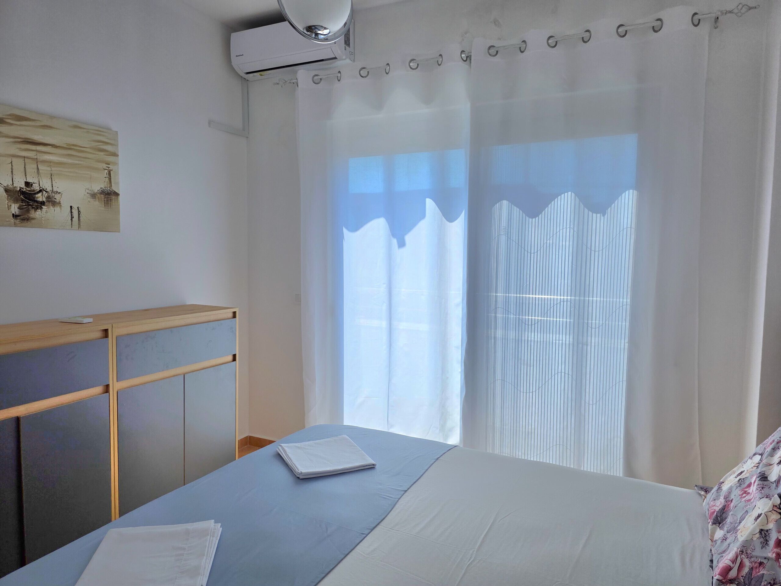 Hotelkamer met een bed, houten hoofdeinde, raam met dunne gordijnen en een airconditioning aan de muur.