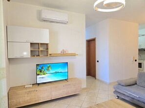 A modern living room with a flat-screen TV, a built-in air conditioner, a wooden cabinet, and a grey sofa.