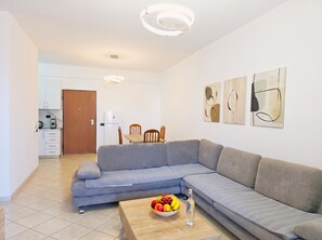 A modern living room with a grey sectional sofa, a wooden coffee table with fruit, and abstract wall art. - Sunny Stay Apartment Durres 080 (Durres)