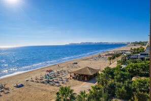 A beach with umbrellas and lounge chairs, a small hut, and a clear view of the sea and distant cityscape. - Sunny Stay Apartment Durres 080 (Durres)
