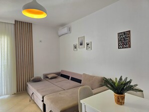 Un salon moderne avec un canapé, une petite table, une plante en pot et un climatiseur fixé au mur.