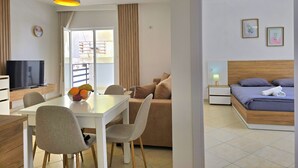 Et moderne hotelværelse med spiseplads, et fjernsyn, en seng med trægavl og en balkon med udsigt.