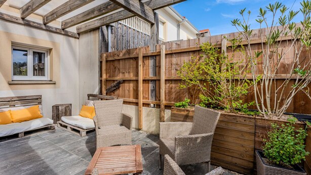 An outdoor patio with wicker furniture, a wooden table, and a wooden fence.