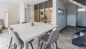 A modern dining area with a white table and grey chairs, a clock on the wall, and a staircase leading to another level.