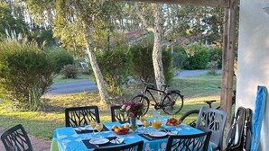 An outdoor dining area with a table set for two, surrounded by chairs, and a bicycle parked nearby. - Cozy house for 6, terrace, residence with pool and parking near the beach (Ondres)