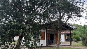 A small, single-story building with a covered porch and a tree in front. - Cozy house for 6, terrace, residence with pool and parking near the beach (Ondres)