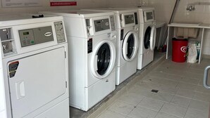 A laundry facility with multiple washing machines and dryers, a red trash bin, and a mop leaning against the wall. - Cozy house for 6, terrace, residence with pool and parking near the beach (Ondres)