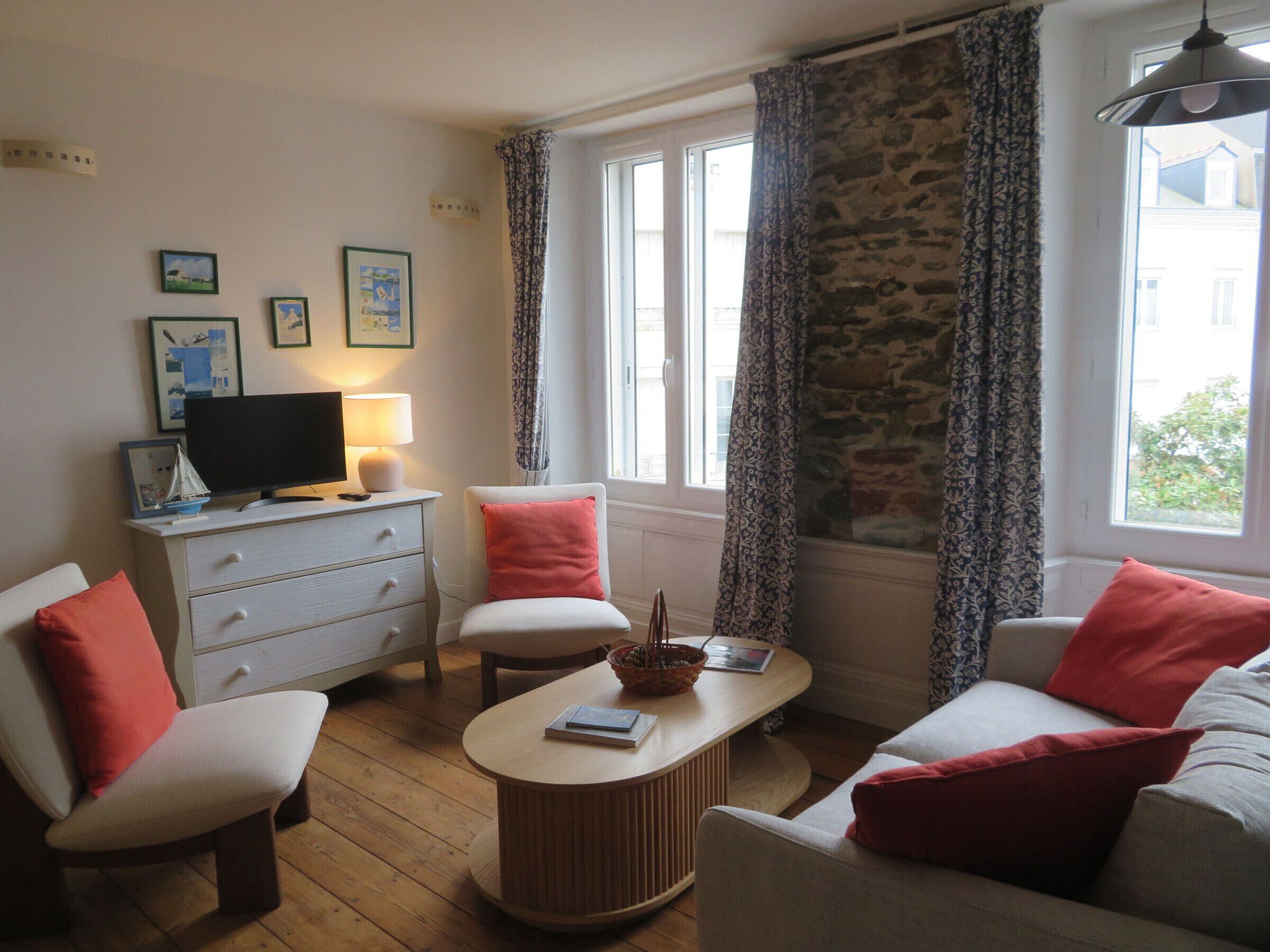 Una habitación con televisión, lámpara, sofá, sillón, mesa y ventana con cortinas.