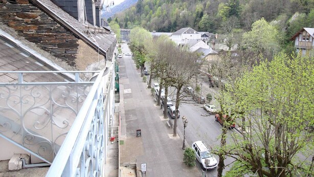 A residential street with houses, a stone wall, and a metal railing.