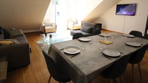 A dining area with a table set for four, a TV mounted on the wall, and a seating arrangement with a sofa and chairs.