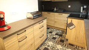 A kitchen with wooden cabinets, a black countertop, a red coffee maker, and a patterned floor.