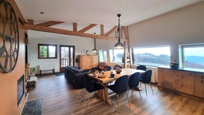 Un vaste espace dédié à la salle à manger, avec une table et des chaises en bois, une grande fenêtre offrant une belle vue et un plafond haut avec des poutres apparentes.