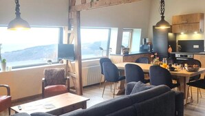 Un salon moderne comprenant un canapé, une table à manger et des chaises. Il y a également un coin cuisine avec une cuisinière, un four à micro-ondes et des placards. De grandes fenêtres offrent une vue sur l’extérieur.