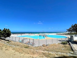 A pool area with a view of the ocean, surrounded by a fence and a dry landscape. - Spacious sea-facing studio with air conditioning (Saint-Martin)