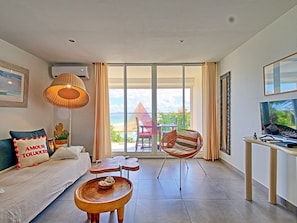 A modern living room with a sofa, a wooden coffee table, a hanging chair, a TV, and a large window with a view of the beach. - Spacious sea-facing studio with air conditioning (Saint-Martin)