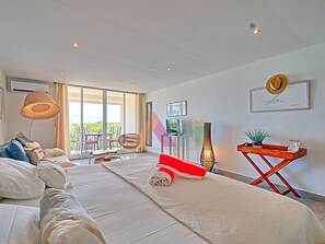 A spacious room with a large bed, a sofa, a dining area, and a view through the glass doors. - Spacious sea-facing studio with air conditioning (Saint-Martin)