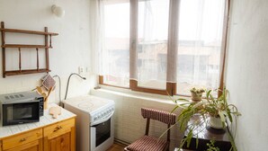 A compact kitchen with a microwave, stove, and wooden cabinets. A window with sheer curtains provides natural light, and a chair is placed near the window. - "bojana", Charming Accomodation in Razlog, Bulgaria (Razlog)