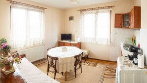 A cozy room with a round dining table, wooden chairs, a television, and a kitchen area with a stove and cabinets. - "bojana", Charming Accomodation in Razlog, Bulgaria (Razlog)