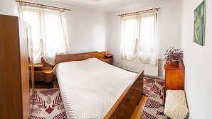 A bedroom with a wooden bed, a nightstand, a radiator, and a window with curtains. - "bojana", Charming Accomodation in Razlog, Bulgaria (Razlog)