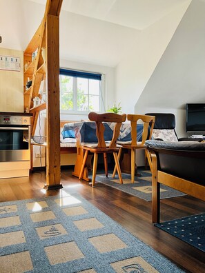 A cozy room with a wooden chair, a sofa, a TV, and a window with a view.