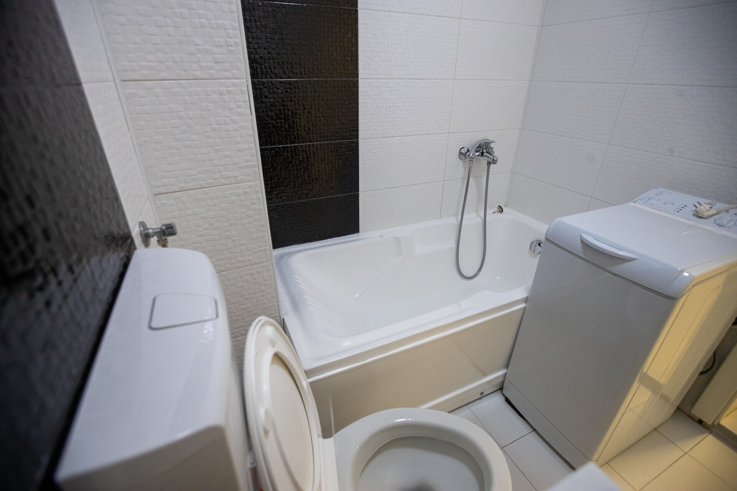 A compact bathroom with a toilet, a bathtub, and a washing machine.