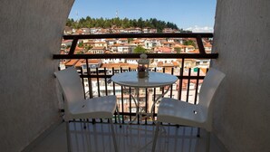 Un balcone con un tavolo bianco e due sedie, che si affaccia su una zona residenziale con edifici a tetti rossi.