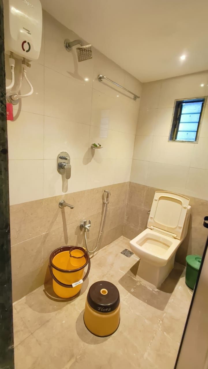 A bathroom with a toilet, shower, and a bucket.