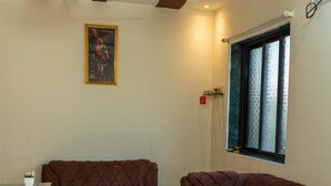 A living room with two brown sofas, a ceiling fan, a framed picture on the wall, and a window with blinds. - Anandvan (Nagaon)