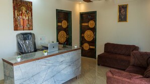 A reception area with a marble counter, a laptop, a plastic chair, and a brown sofa. - Anandvan (Nagaon)