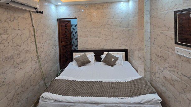 A bedroom with a bed, ceiling fan, air conditioning unit, and marble walls. - Shri Ganga Palace (Faizabad)