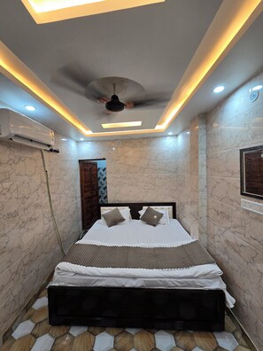 A bedroom with a bed, ceiling fan, air conditioning unit, and marble walls. - Shri Ganga Palace (Faizabad)