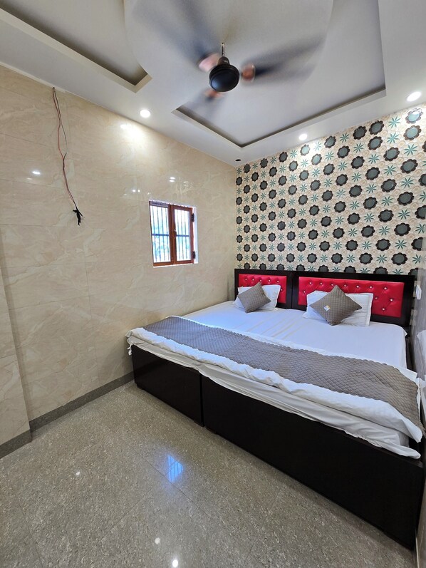 A bedroom with a bed, a ceiling fan, a window, and a patterned wall. - Shri Ganga Palace (Faizabad)